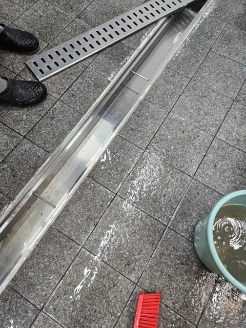 스테인리스 배수로 덮개와 주변 타일 바닥을 세척하는 모습