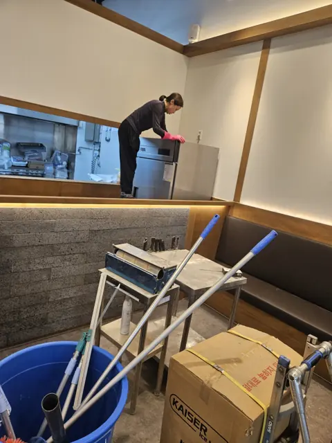 카운터 뒤 조리 공간을 청소하는 작업자와 청소 도구