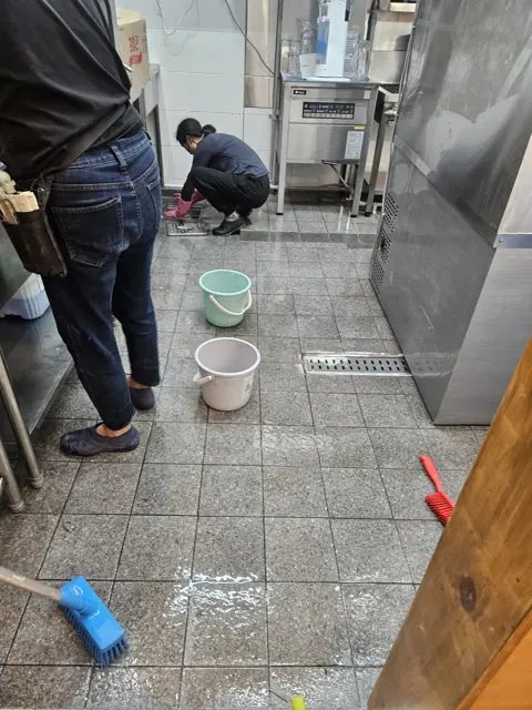 주방 바닥 타일을 쪼그려 앉아 솔로 닦는 작업자